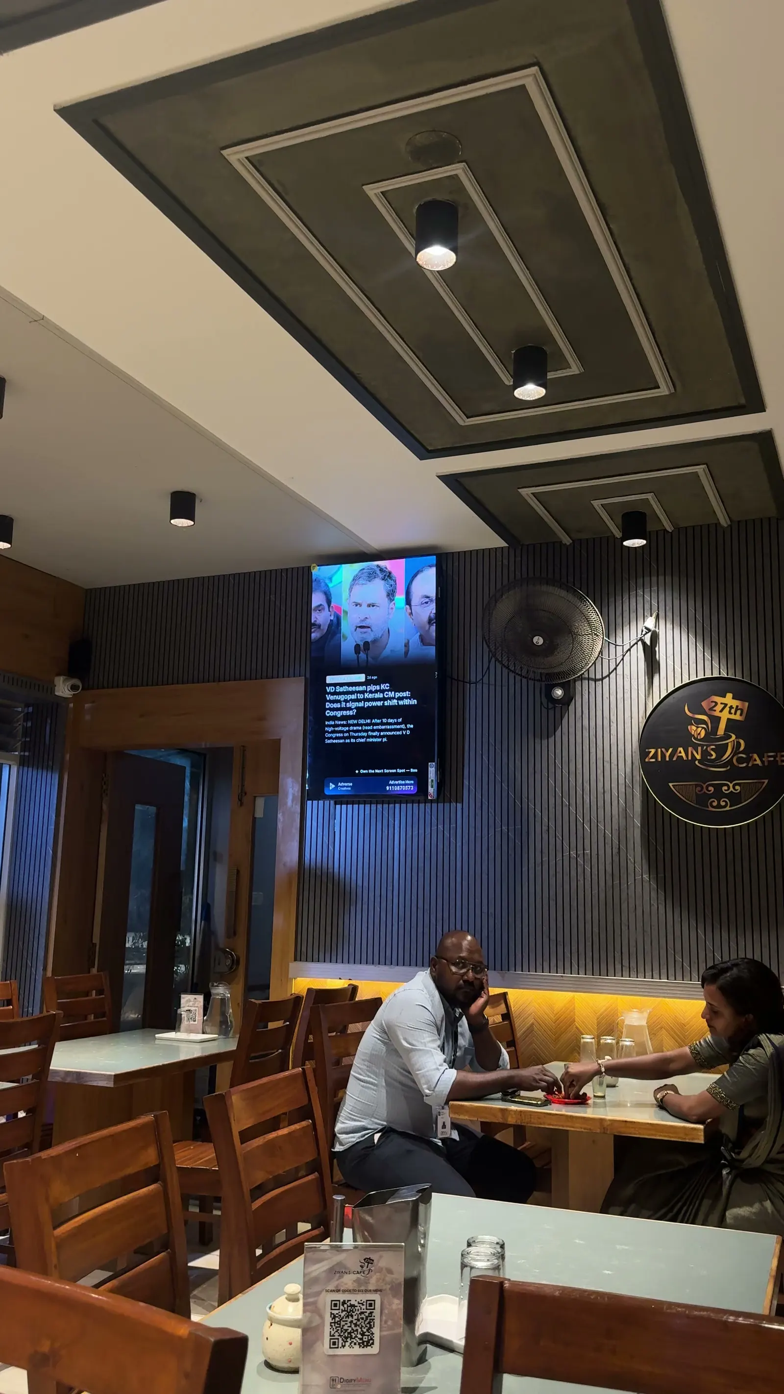 Guests at a café table beneath an AdVerse screen showing live news