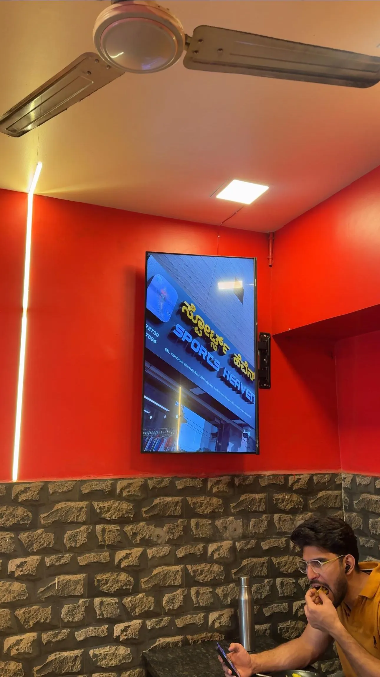 An AdVerse screen on the red wall of CM Foods Restaurant, BTM, while a diner eats below
